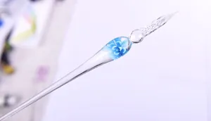 Detail shot of a handmade glass dip pen featuring an intricate blue floral inlay.