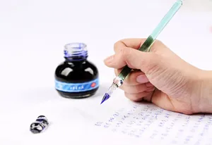 Detailed shot of a green glass dip pen writing on paper with blue ink