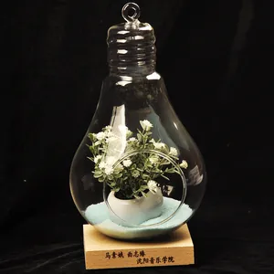 Creative bulb-shaped glass terrarium vase with artificial flowers on a wooden base