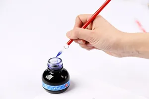 Detailed close-up of a red handmade glass dip pen being dipped into blue ink
