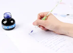 Close-up of an elegant green threaded glass dip pen writing with blue ink on paper.