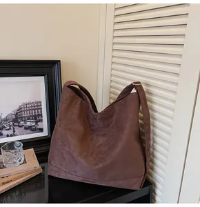 Detailed view of a brown suede slouchy shoulder bag on a stylish tabletop setup with art.