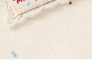 Primo piano dettaglio di top in maglia per ragazze con patch ricamata e volant beige.