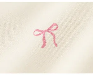 Grazioso dettaglio di fiocco rosa ricamato su morbido tessuto a maglia bianca primo piano.