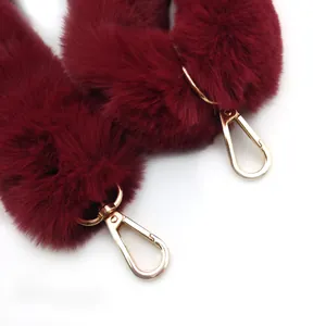 Primer plano detallado de la correa de bolso de peluche burdeos con hebillas doradas.