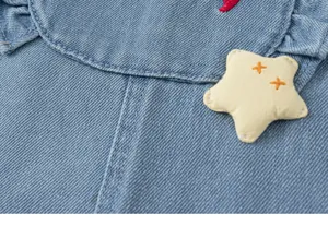 Gros plan détail de salopette en jean pour fille, joli patch étoile et poche douce.