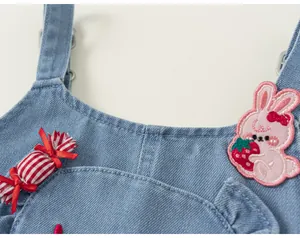 Gros plan de la sangle de salopette en denim pour fille avec broderie lapin et fraise mignonne.