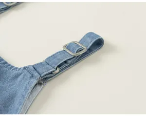 Gros plan détail de la sangle réglable de salopette en jean avec boucle métallique.