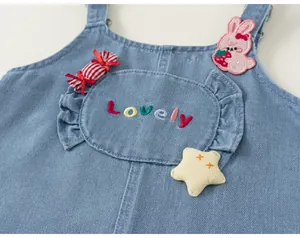 Détail de salopette en denim pour fille avec broderie de dessin animé et inscription.