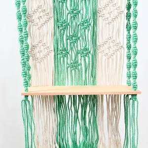 Bohemian macrame wall hanging shelf with green and beige woven cotton cords and wooden board.