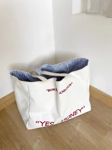 Canvas tote bag detail showing embroidered red text and blue striped lining interior.