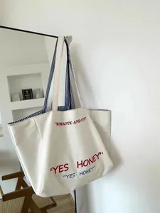 Canvas tote bag for women, large capacity shoulder bag with stylish embroidered text and stripes.