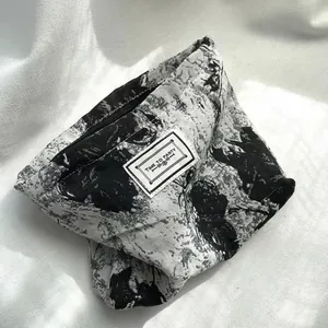 Detail of black and white abstract print cosmetic pouch with zipper and woven text label.