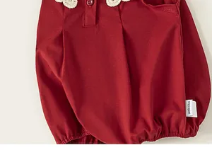 Vue détaillée de la robe rouge pour bébé, dotée d'un col en dentelle et de charmants boutons.