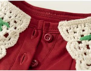 Gros plan détail col de robe fille rouge, bordure en dentelle crochet blanche, boutons.