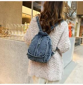 Detail der verwaschenen Denim-Struktur eines modischen Rucksacks über einem Strickpullover.
