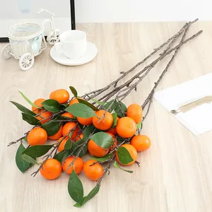 Detailaufnahme künstlicher Orangen-Zweige mit grünen Blättern und leuchtenden Deko-Früchten.