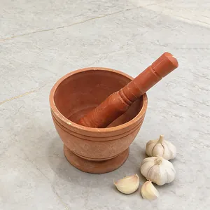 Detailopname van een terracotta vijzel en stamper met verse knoflook op een marmeren blad.
