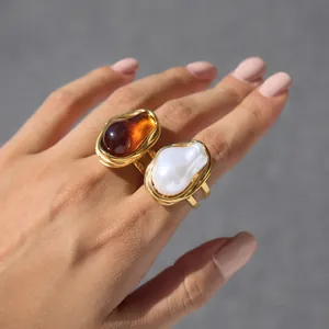 Détail de bagues en acier titane doré avec perle baroque et résine ambre de haute qualité.