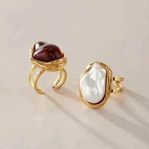 Gros plan de bagues en acier titane doré avec perle baroque et pierre en résine rouge.