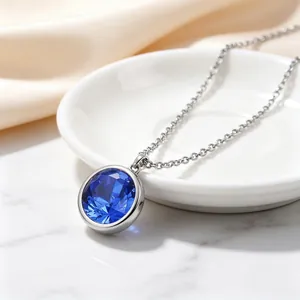 Primer plano de un collar de acero de titanio con una piedra redonda azul facetada.
