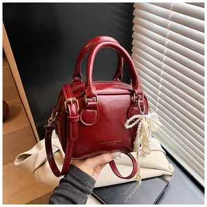 Detail view of a luxury red leather handbag with a pearl bow charm and top handles