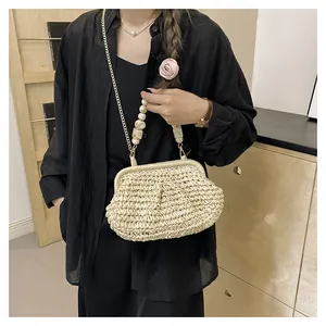 Dettaglio di pochette in paglia intrecciata con manico di perle e catena d'oro su modella