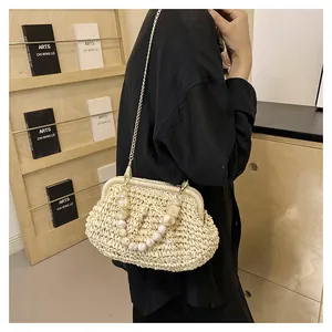 Dettaglio di borsa in paglia intrecciata con manico di perle e catena in metallo fine