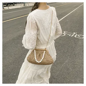 Dettaglio di pochette in paglia intrecciata con manico di perle e catena dorata