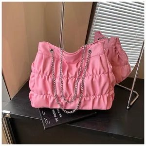 Stylish pink ruched tote bag with silver chain straps presented on a dark desk
