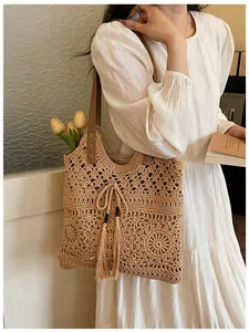 Vista detallada de un bolso tote de ganchillo de algodón beige con diseño calado y borlas.