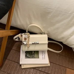 Λεπτομερής λήψη κομψής κρεμ τσάντας χειρός με μεταλλικό κλείωμα και κρεμαστά σε βιβλία.