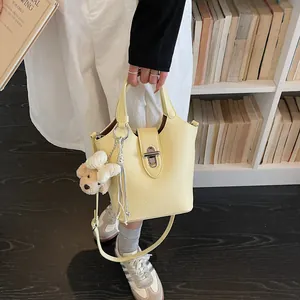 Chic yellow leather bucket bag with metal lock and cute bear charm for women summer daily.