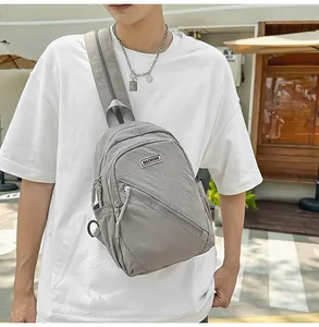 Gros plan détaillé du sac bandoulière en nylon gris avec poches zippées et badge.