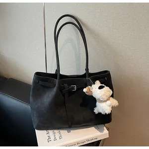 Detalle de un bolso tote grande vintage negro con un colgante de perro de peluche en un libro
