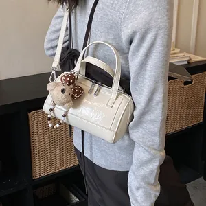 Detailed view of white patent leather cylindrical Boston bag with cute bear charm and handles.