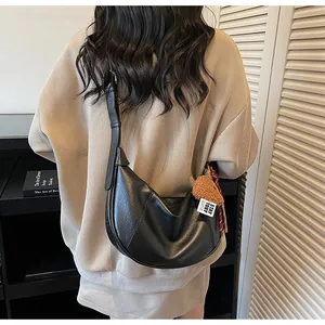 Chic black leather hobo shoulder bag with trendy dumpling shape and cute bear pendant.