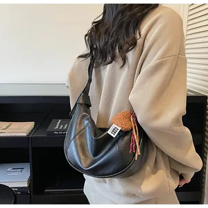 Close-up view of the black slouchy shoulder bag with cute plush heart charm and strap detail.