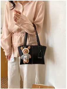 Black underarm tote bag detail with contrast stitching and cute plush bear charm.