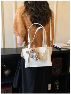Detailed view of women white leather shoulder tote bag with cute plush bear charm and handles.