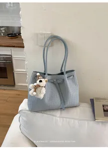 Elegante hellblaue geflochtene Tragetasche mit einem dekorativen Teddybär-Anhänger