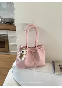 Elegante rosa gewebte Schultertasche mit Bärchen-Anhänger in modernem Interieur