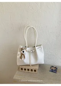 Detail einer weißen geflochtenen Tragetasche mit süßem Bären-Schlüsselanhänger-Dekor.