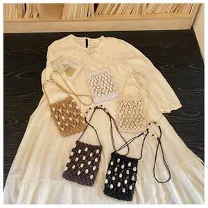 Bolsos bandolera de paja tejida con detalles de conchas sobre un vestido de verano crema