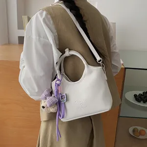 Detailaufnahme einer schicken weißen Eimer Tasche mit rundem Griff und Bärenanhänger.