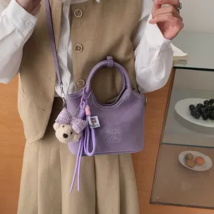 Nahaufnahme der stilvollen lila Beuteltasche mit süßem Bärenanhänger und Prägung.