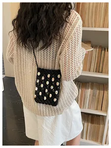 Detailed view of black crochet phone bag with shell beads on a casual outfit