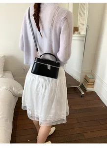 Elegante zwarte doosvormige crossbodytas gedragen door een model in een slaapkamer.
