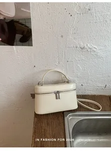 Detail van crèmekleurige boxhandtas met zilveren rits op houten tafel