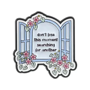 Close-up detail of the creative window shaped enamel pin with pink floral vines and quote text.